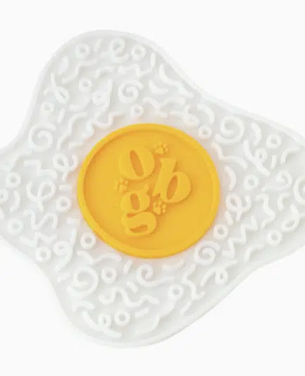 Tapis de léchage pour chien Ollie B. Good en forme d’œuf au plat, silicone alimentaire jaune et blanc.